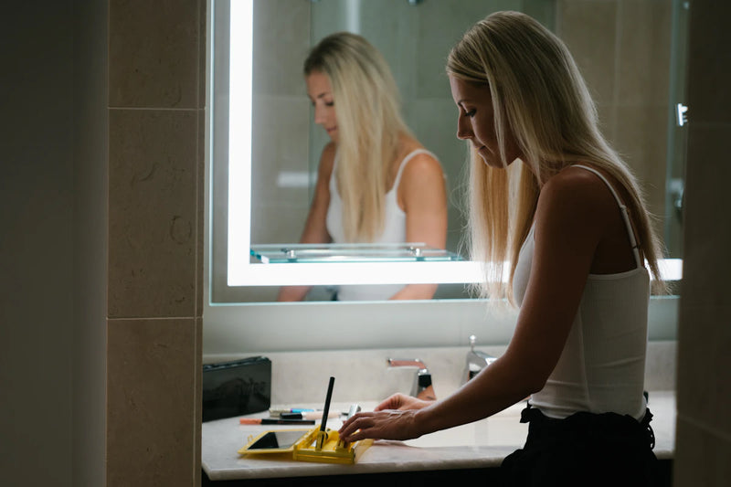 Woman in a white tank top standing in front of a bathroom mirror