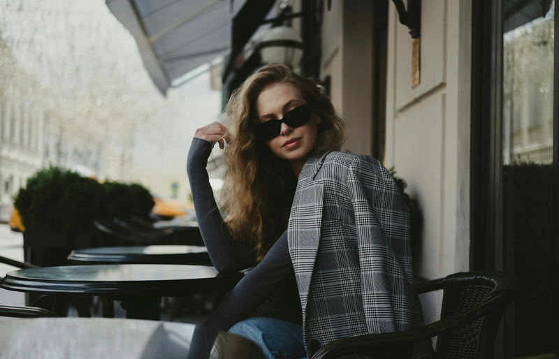 An elegant woman in modern attire seated in front of a sophisticated building, looking poised and considered