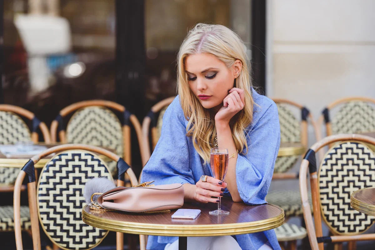 Stylish woman at a Parisian cafe table with a glass of rose and her phone beside her