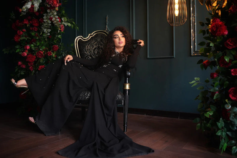 Woman in an elegant black dress seated in an ornate chair surrounded by red roses